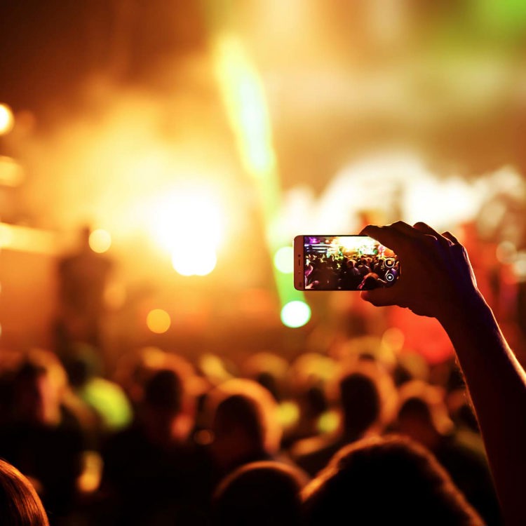 Bild på en hand med en mobiltelefon som spelar in live på en musikfestival.