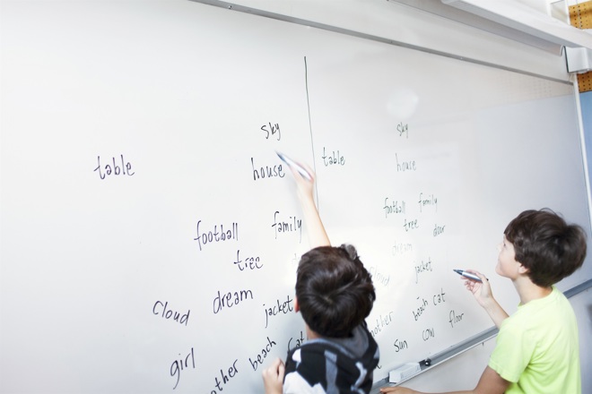 Två barn skriver engelska ord på whiteboardtavla i klassrum