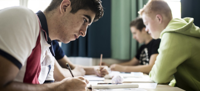 Gymnasielever sitter vid bord och skriver