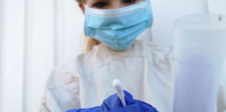 En person med munskydd håller i en bomullspinne med sina handskar.